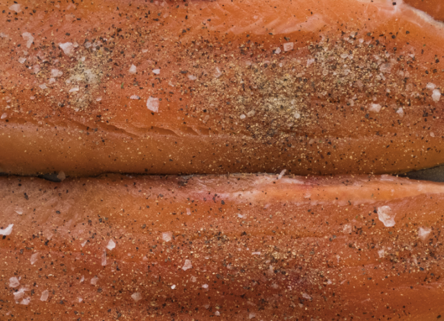 A closeup of lake trout fillets that have been seasoned with salt and pepper on a baking sheet.